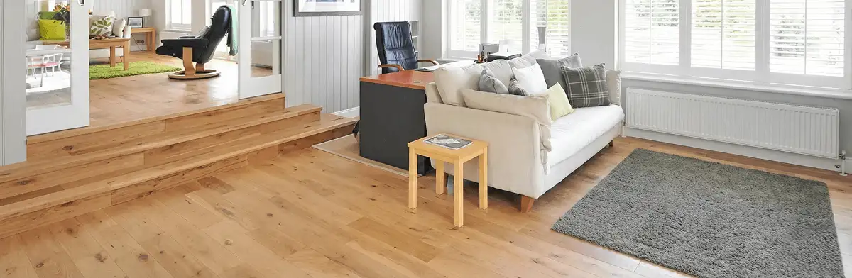 A modern living room with professionally installed laminate flooring, a beige sofa, a small side table, a gray rug, and large windows with white shutters in Albuquerque, NM
